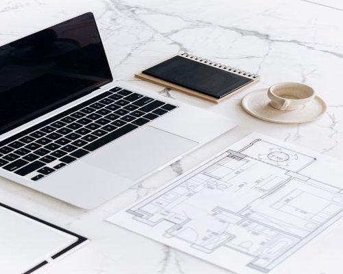 Ergonomic workspace at home showing a laptop, notebook, and a cup of coffee