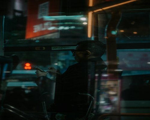Person holding a smartphone looking outside a bus window during an urban commute